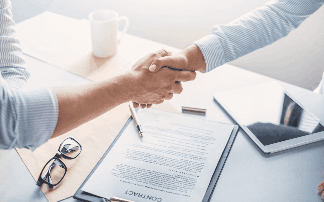 Two professionals shaking hands over a construction contract on a desk.
