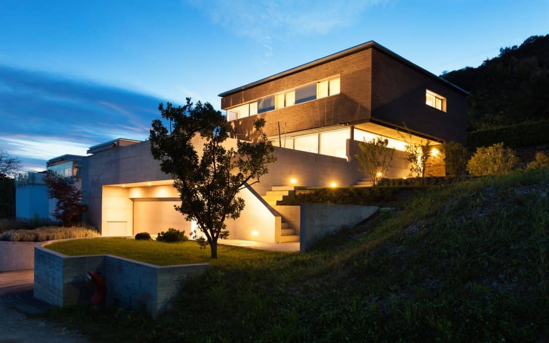 Contemporary hillside house with illuminated exterior lighting and landscaped yard.