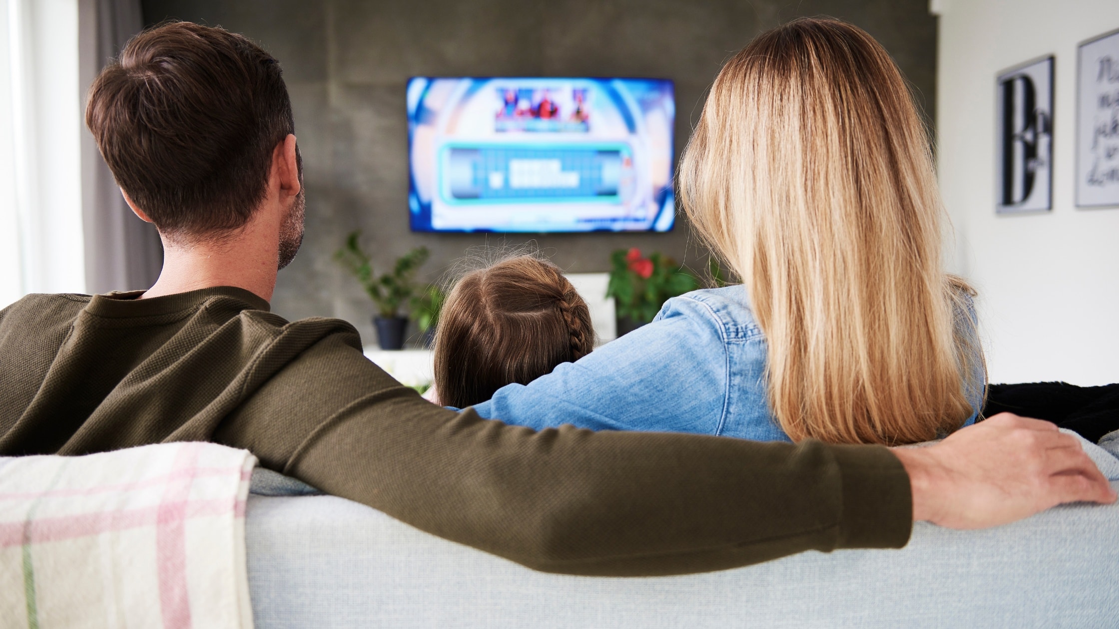 Family relaxing on sofa watching TV together in living room.