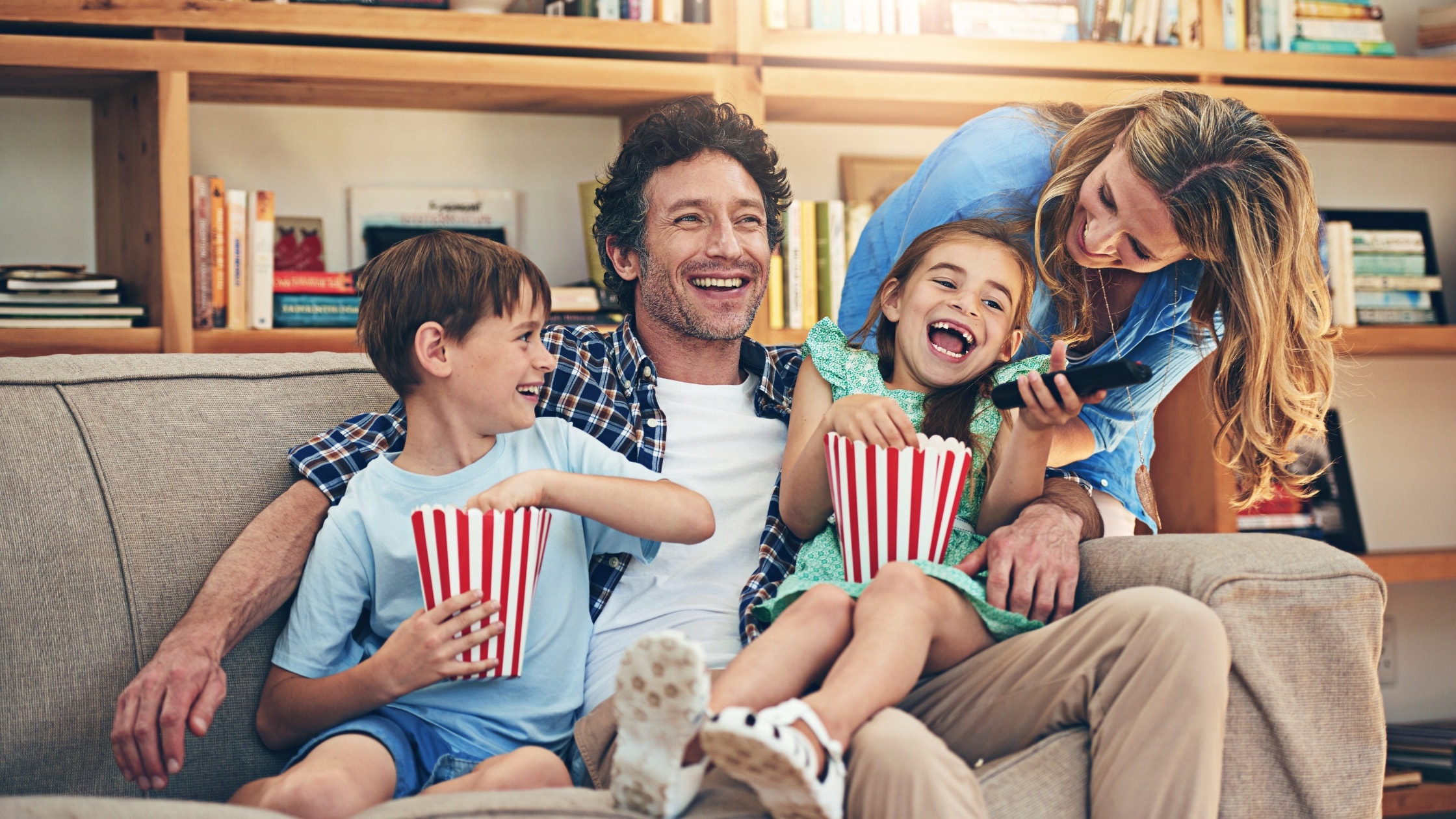 Happy family enjoying a movie together on a sofa with popcorn and snacks.