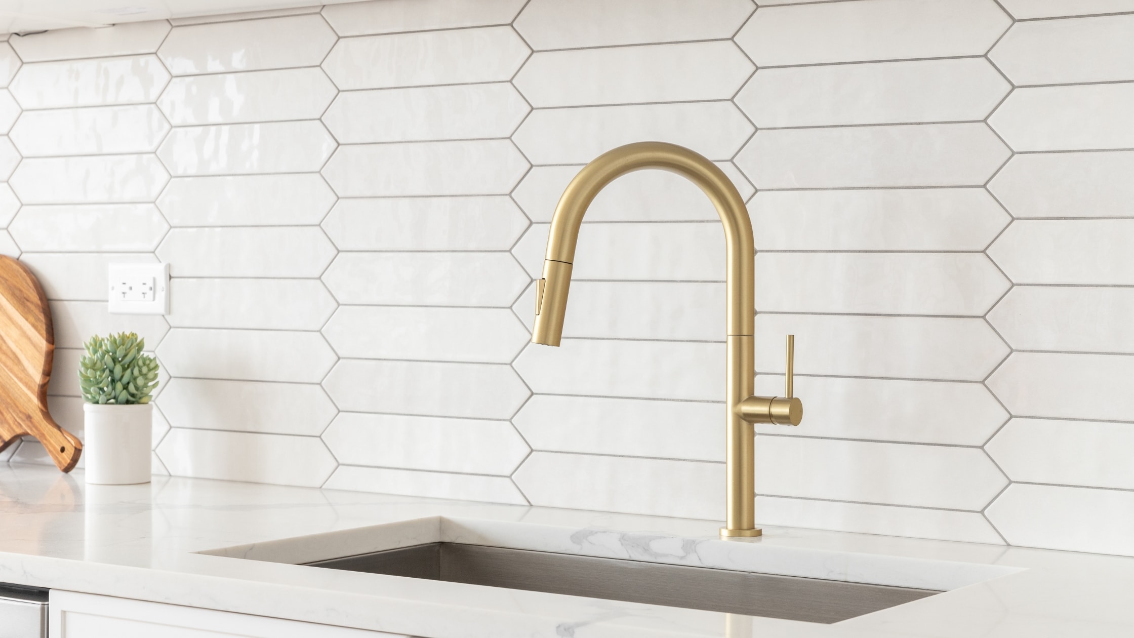 Modern kitchen sink with gold faucet and white hex tile backsplash.