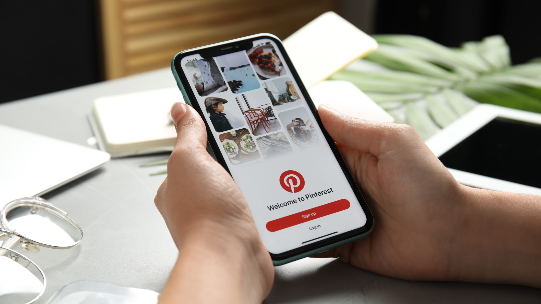 Person holding smartphone displaying Pinterest app on a clean workspace.