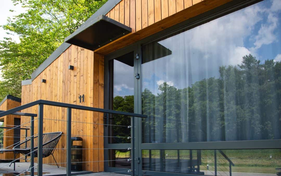 Modern wooden cabin with large glass windows and outdoor seating area.