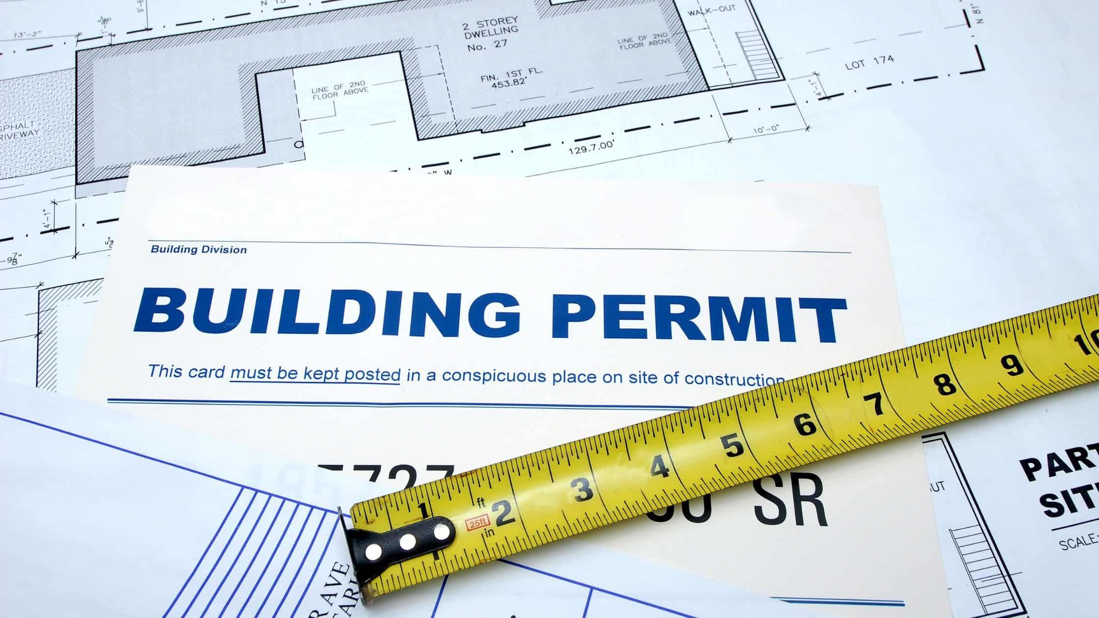 Building permit document with measuring tape on blueprints.