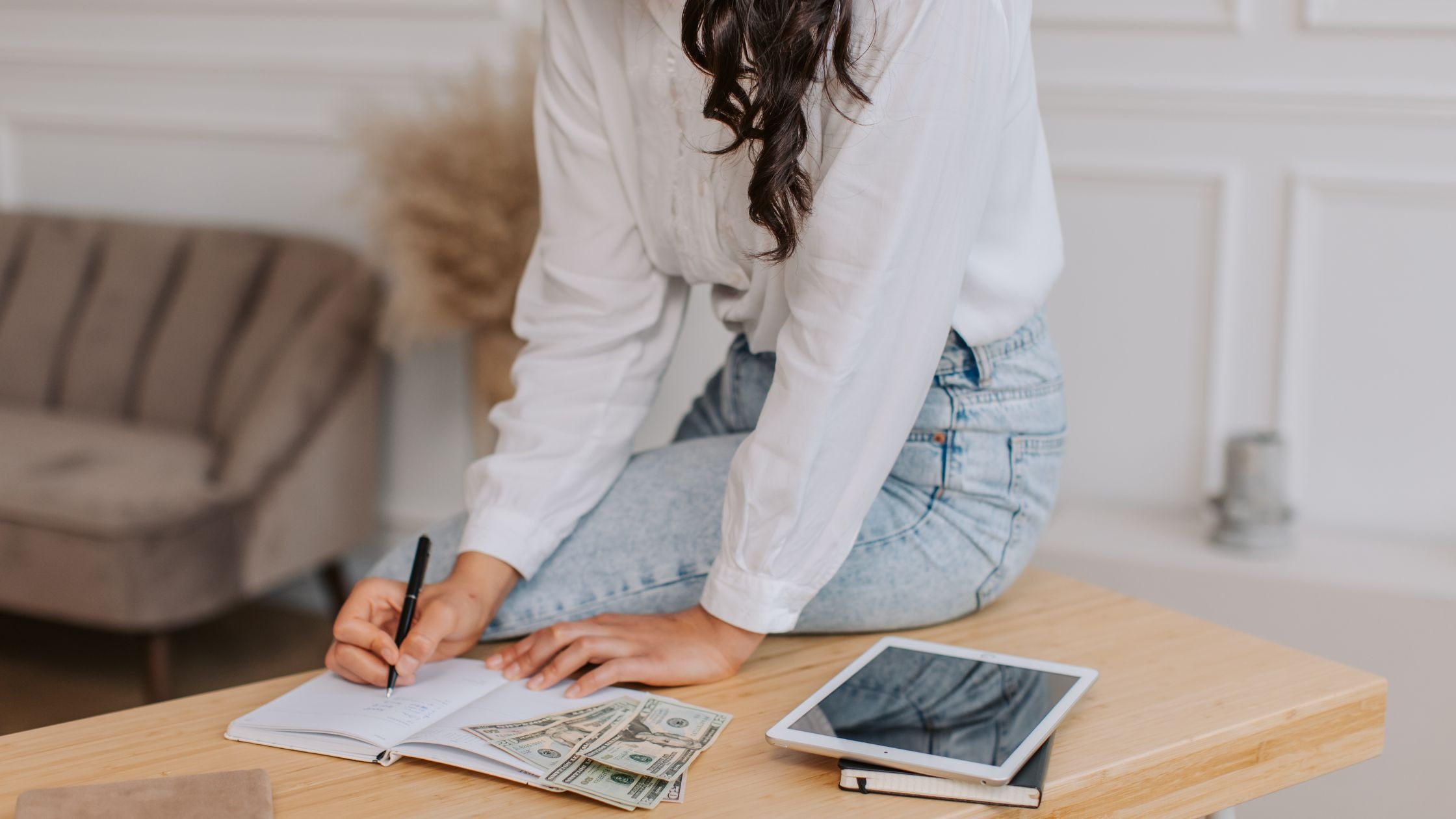 Woman working at a home office with a notebook, tablet, and cash, showcasing residential renovation.
