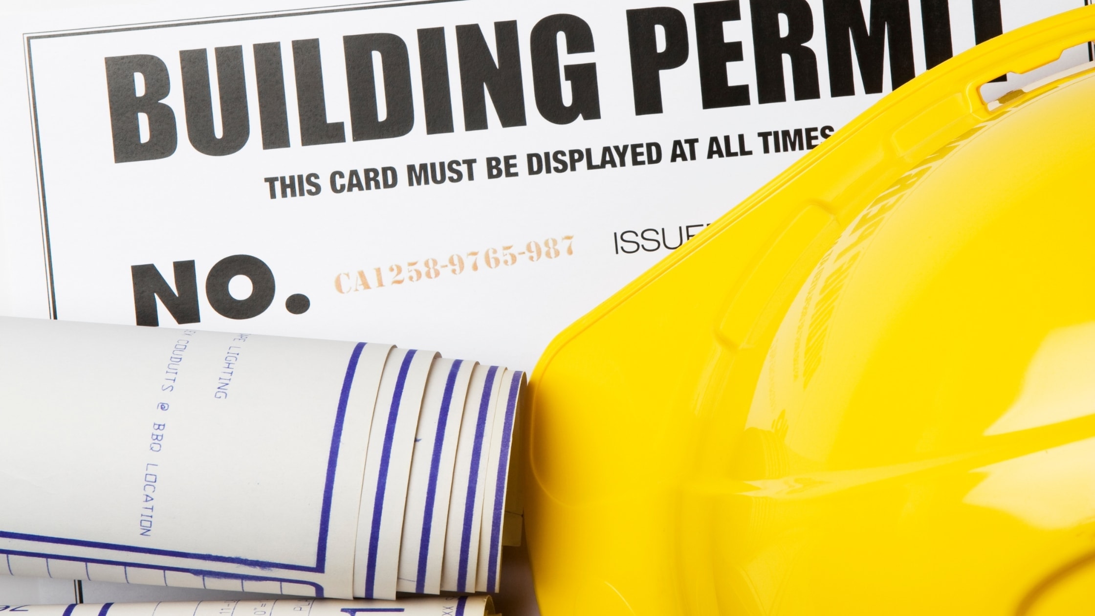 Building permit card with yellow safety helmet and rolled blueprints.