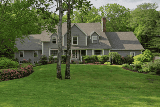 Beautiful gray house with lush green lawn and mature trees, showcasing quality construction and land.