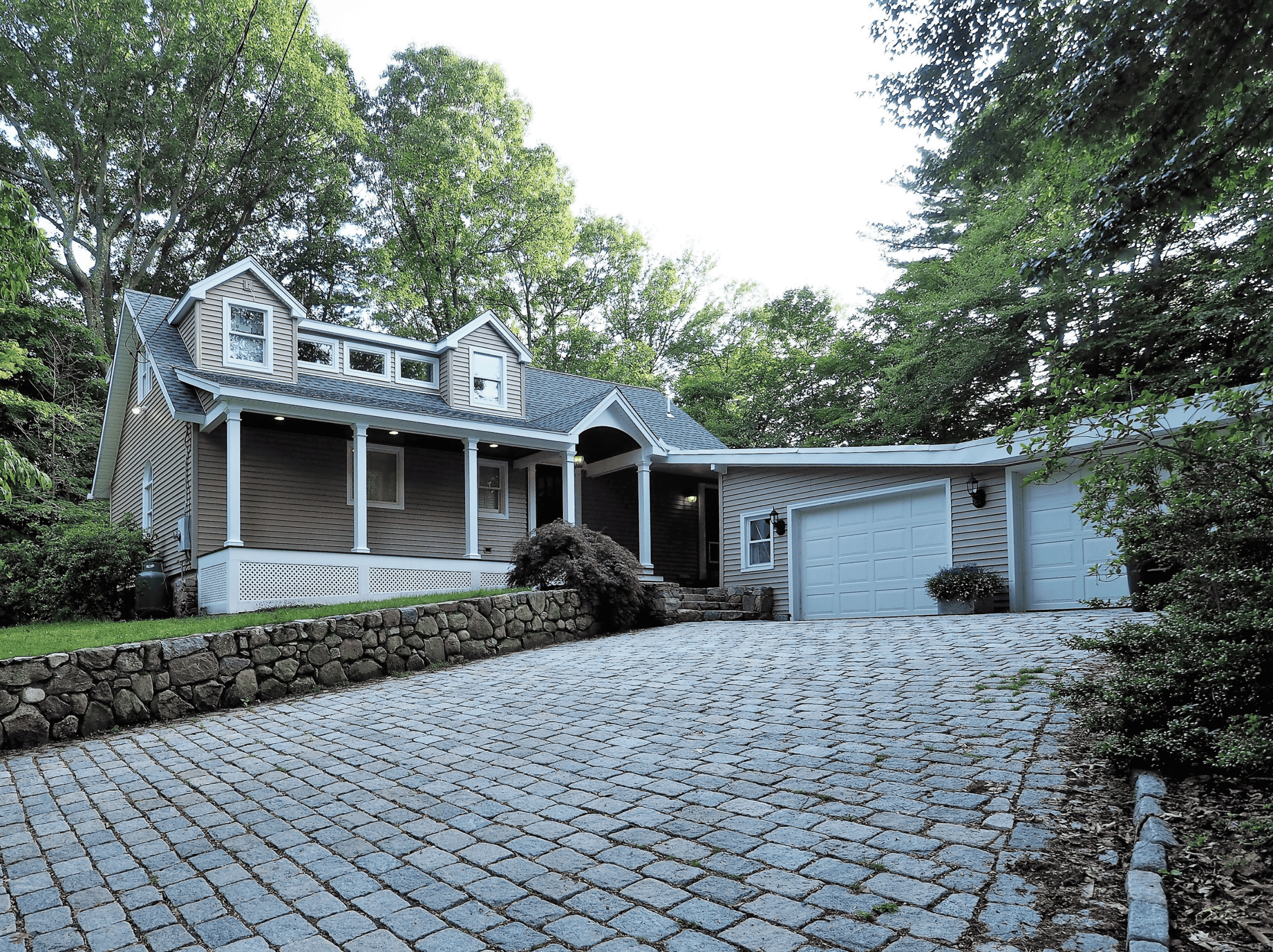 Beautiful modern craftsman-style house with a stone driveway and lush greenery.