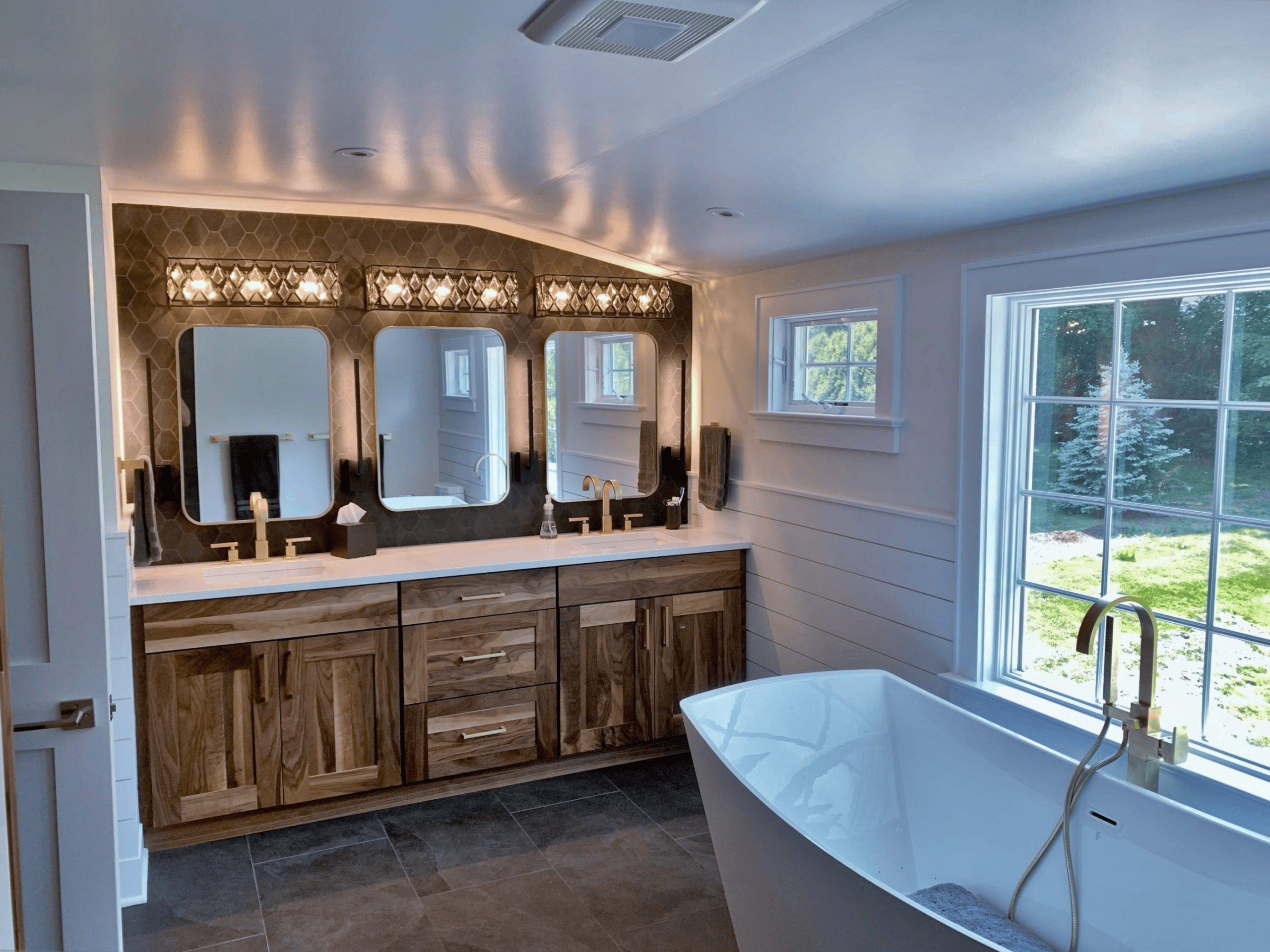Elegant bathroom with double vanity, stylish mirrors, and a soaking tub near large windows.