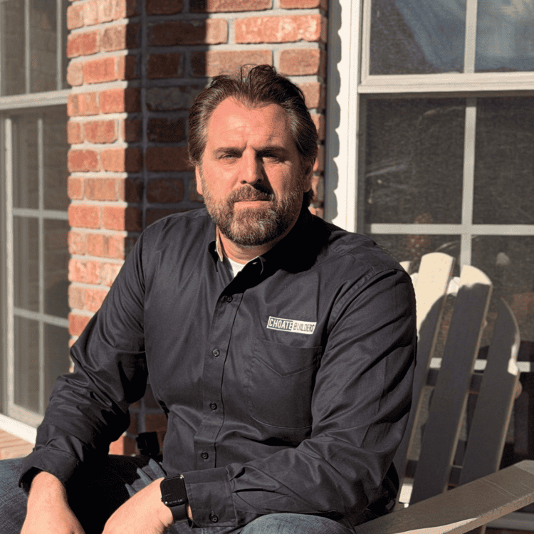 Construction professional sitting outdoors in front of a brick building, wearing a black shirt with.