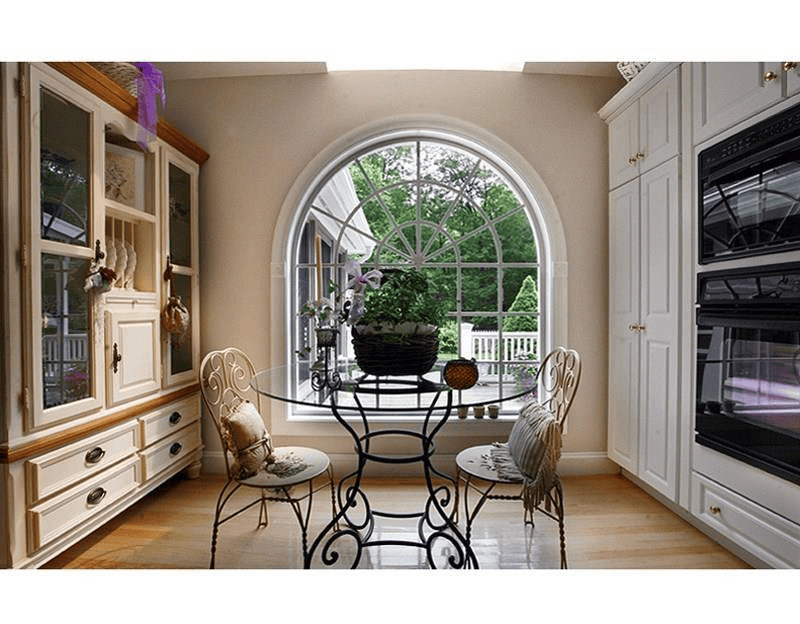 A cozy kitchen nook with a round window, glass table, and elegant chairs, perfect for enjoying meals.