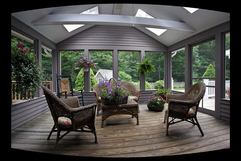 Sunroom with wicker furniture and potted plants, overlooking a lush green backyard.