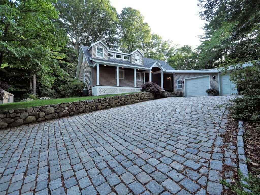 Beautiful house with a cobblestone driveway surrounded by lush greenery and mature trees.