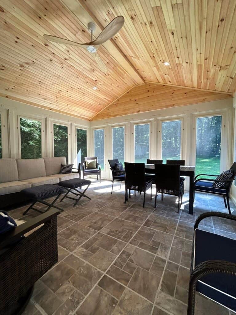 Bright sunroom with large windows and wooden ceiling.