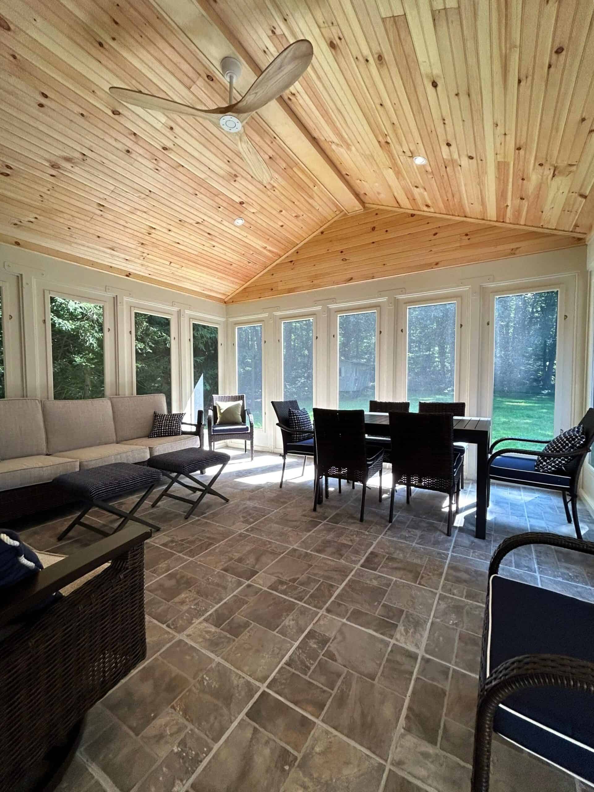 Bright sunroom with large windows and wooden ceiling.