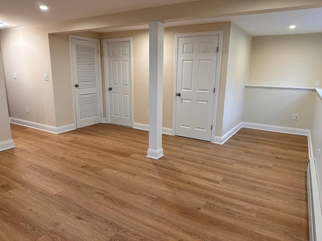 Modern basement with hardwood flooring, white doors, and neutral walls.