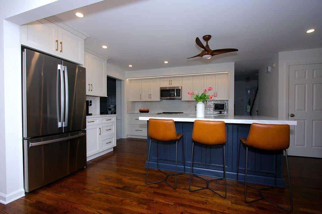 Modern kitchen with white cabinets, stainless steel appliances, and a blue island with orange bar st.