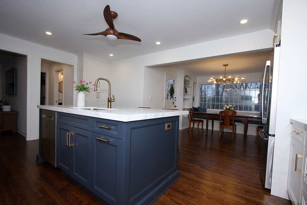 Modern kitchen with blue island, white countertops, and open dining space with large windows and cha.