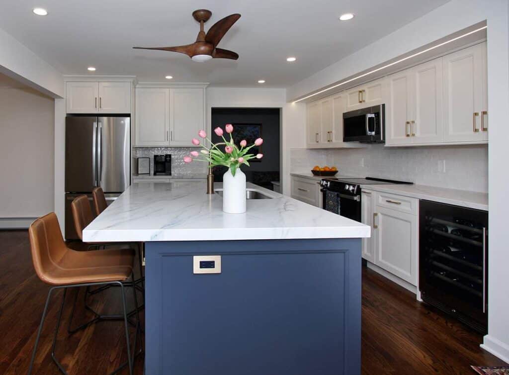 Modern kitchen with white cabinets and a blue island, featuring a marble countertop and stainless st.