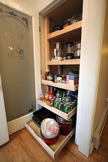 Organized kitchen cabinet with shelves holding small appliances, canned goods, and kitchen essential.