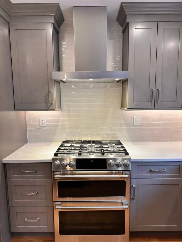 Modern kitchen featuring stainless steel stove, gray cabinets, and white backsplash.