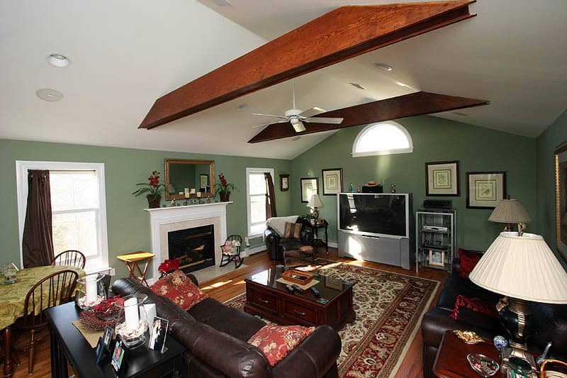 Spacious living room with green walls, wooden beams, and cozy furniture setup.