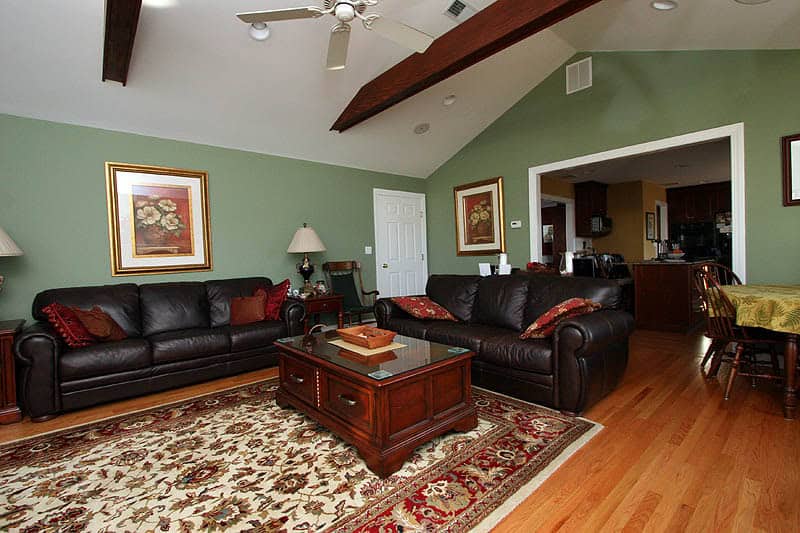 Living room with green walls, leather sofas, and wooden furniture. Bright, inviting space with artwo.
