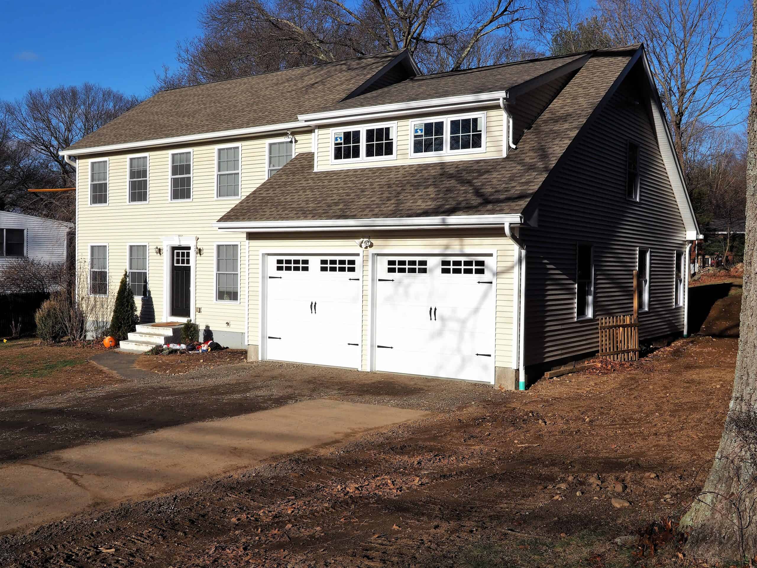 New construction home with double garage, beige siding, and large windows, under a clear blue sky.
