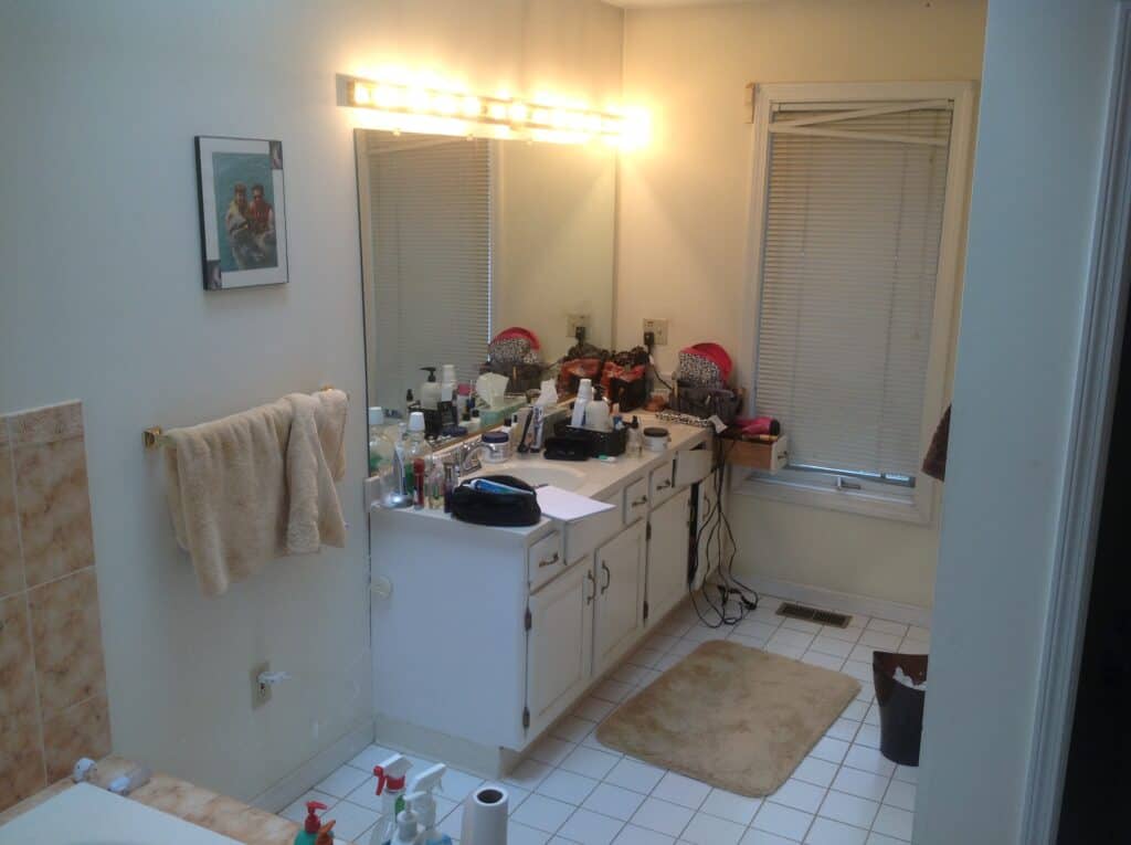 Bathroom vanity with cluttered countertop and mirror, towels, and personal items.