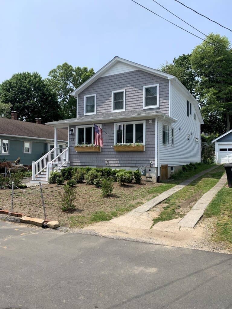 Modern two-story house with front porch and landscaped yard in a suburban neighborhood.