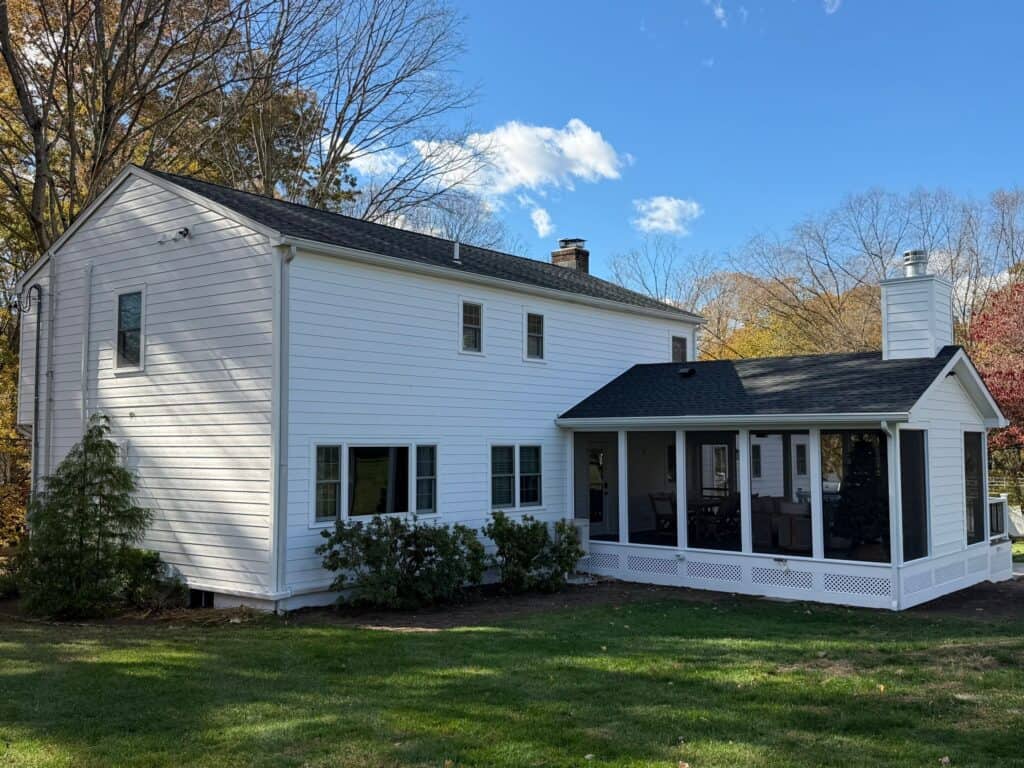 White two-story house with a screened porch and black roof.