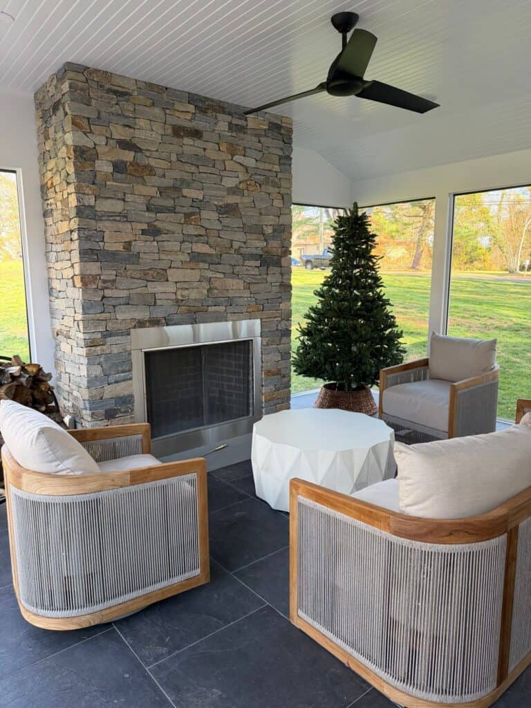 Bright sunroom featuring a stone fireplace and a decorated Christmas tree. Comfortable seating creat.