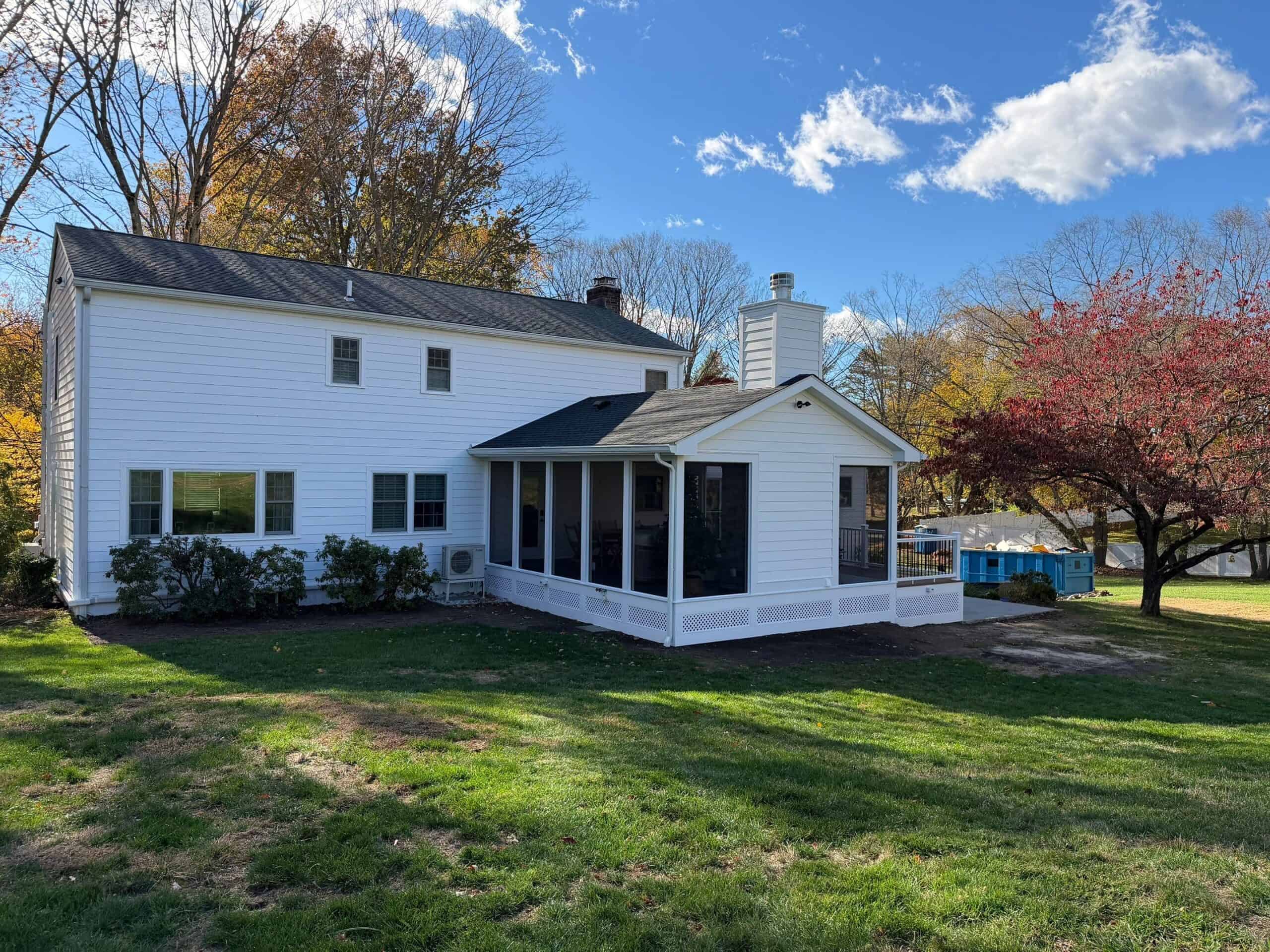 Sunroom addition to a classic white house with large windows and a spacious backyard.