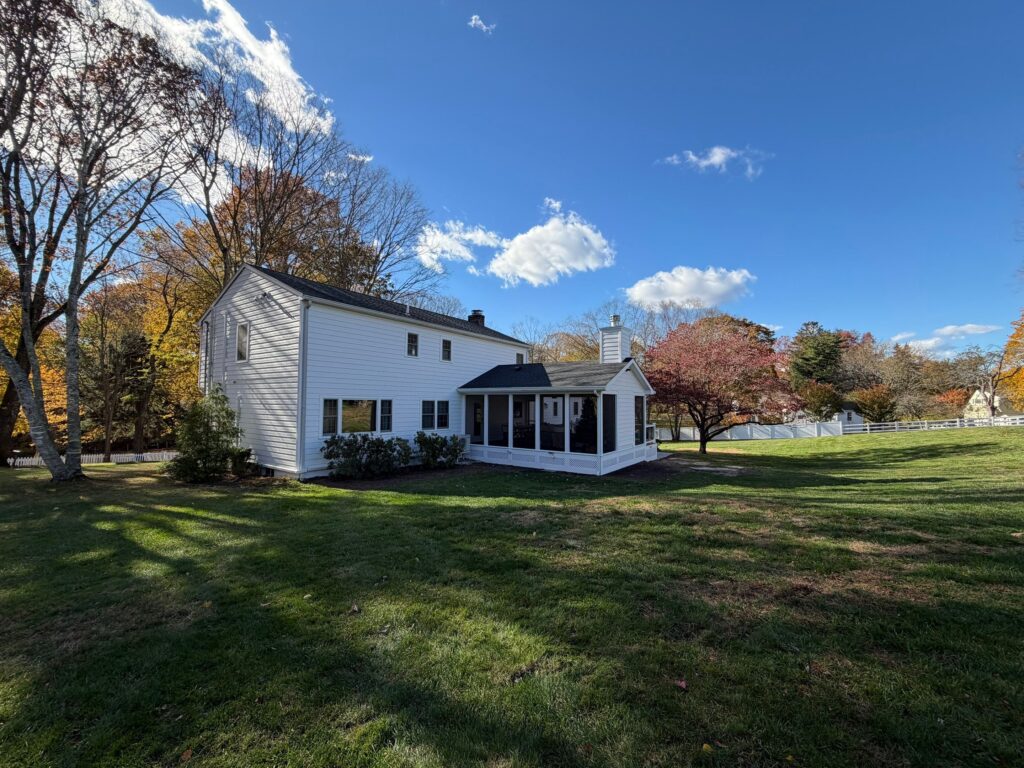 Beautiful white house with a spacious backyard and colorful trees in a suburban neighborhood.
