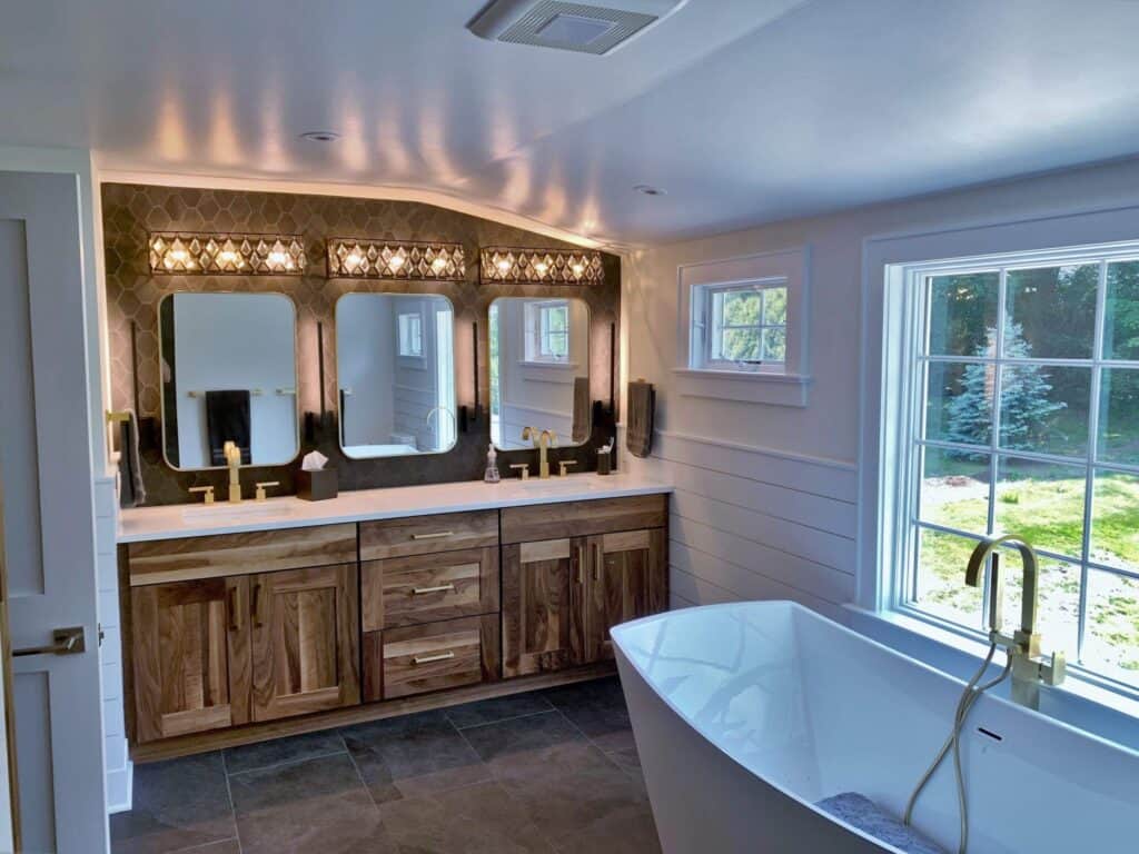 Elegant bathroom with wooden vanity, large mirrors, and a freestanding bathtub by the window.