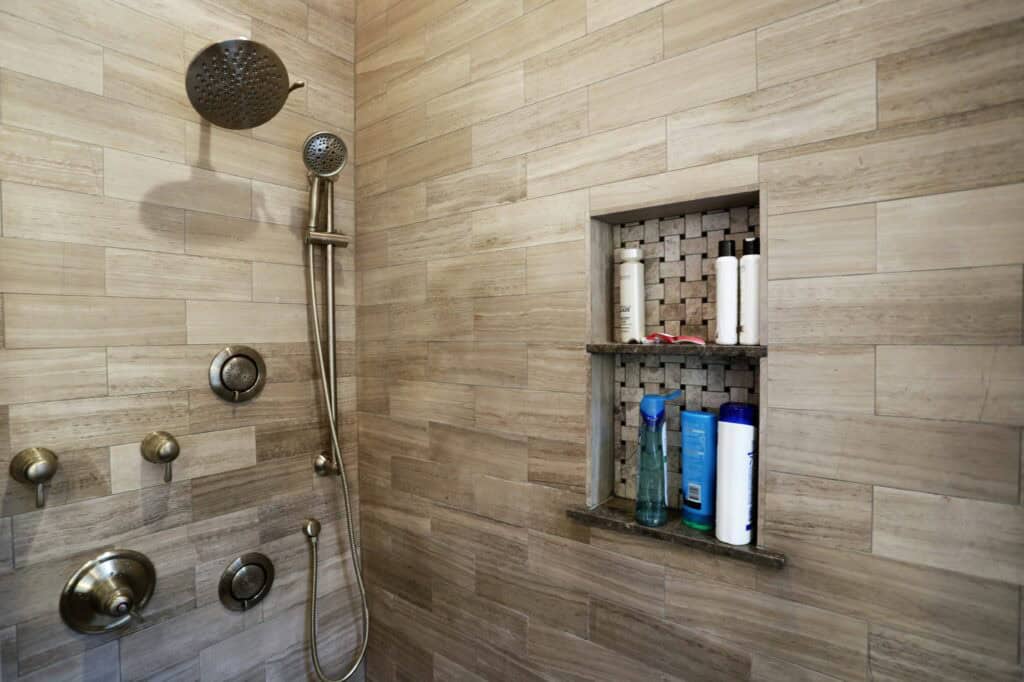 Elegant shower with beige stone tiles and built-in niche for toiletries.