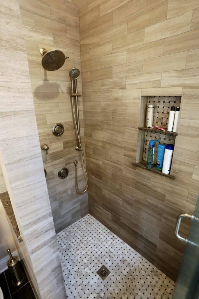 Accessible shower with rainfall and handheld showerheads, tiled walls, and built-in niche for toilet.
