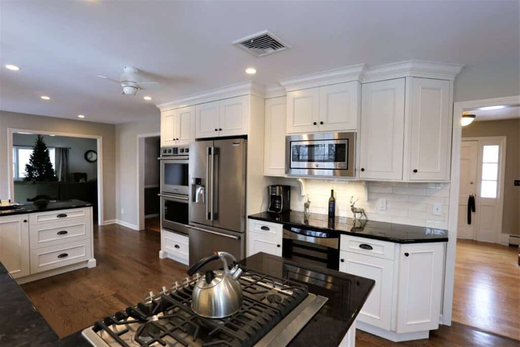 Bright modern kitchen with white cabinets, stainless steel appliances, and black countertops.