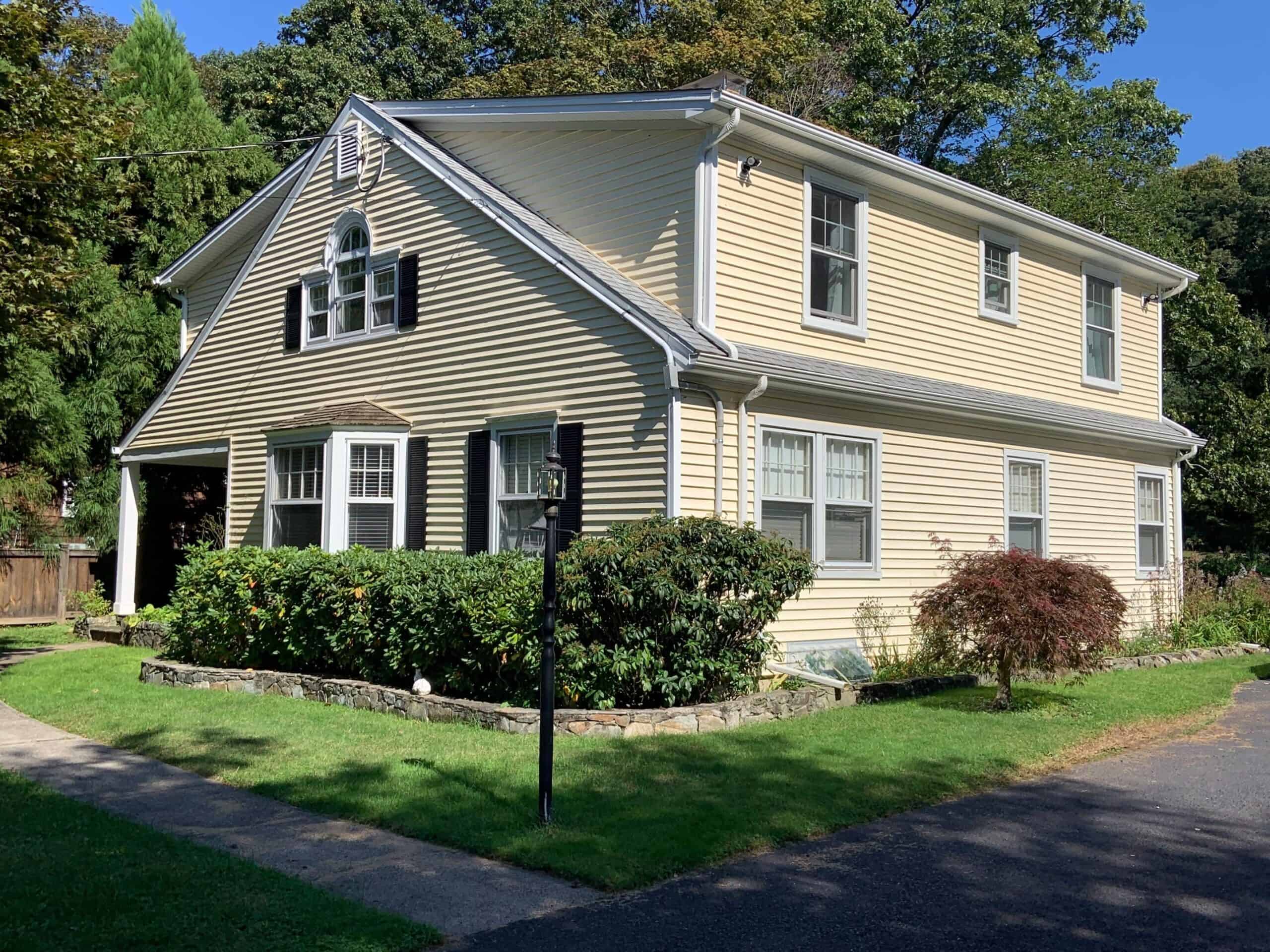 Beautiful two-story house with beige siding, white trim, and lush landscaping.