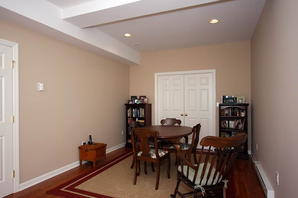 Interior view of a cozy dining room with wooden table and chairs, beige walls, and built-in bookshel.