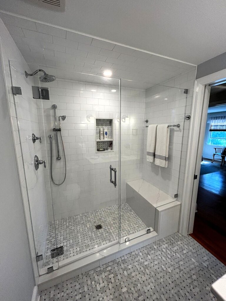 Walk-in shower with glass enclosure and multiple showerheads.