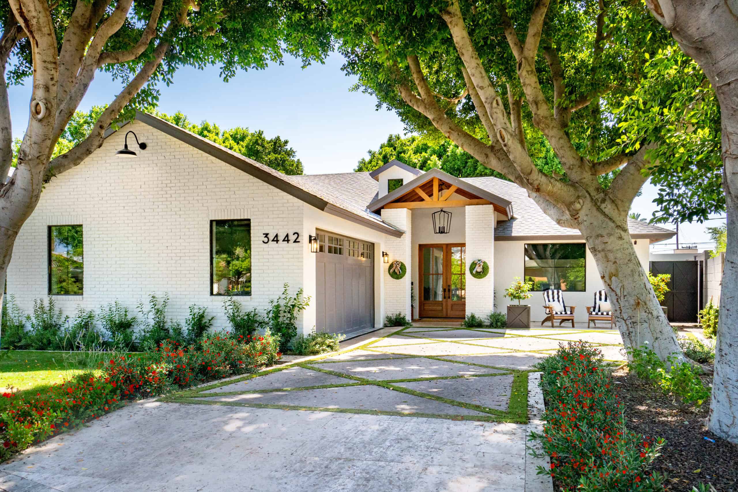 Beautiful modern house with white exterior, large trees, and landscaped yard in a sunny setting.