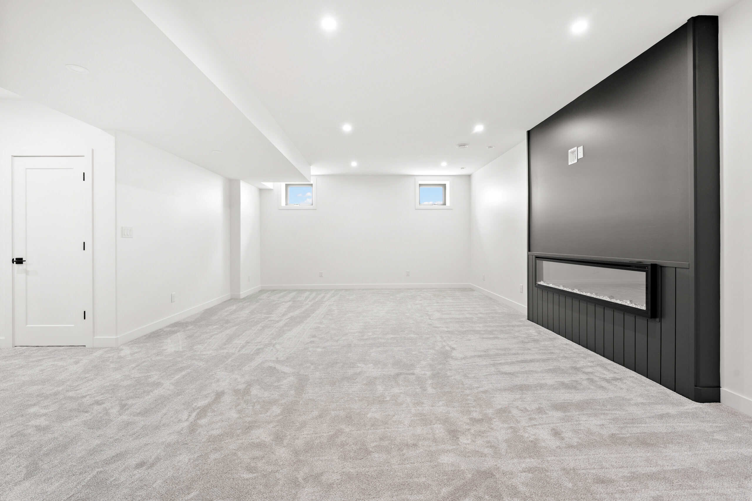 Spacious finished basement with white walls, gray carpet, and a black accent wall with a fireplace.